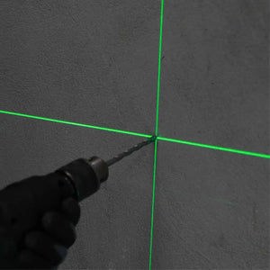 Green laser level tool projecting crosshair lines on dark concrete wall surface with black handle visible in foreground