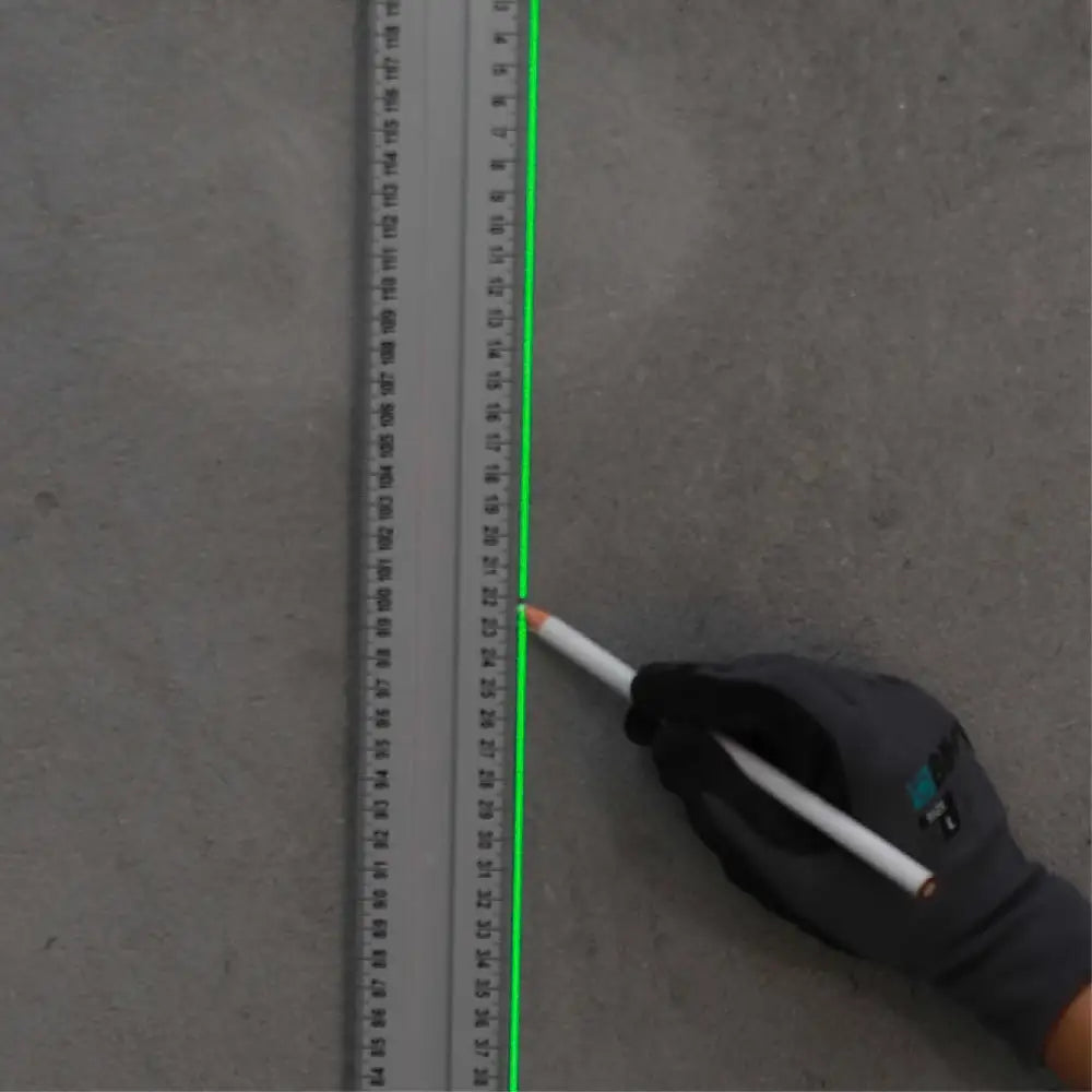 Bihui self-leveling laser level BHLLG05 projecting bright green laser line onto concrete floor next to measuring tape, held by gloved hand wearing black work glove