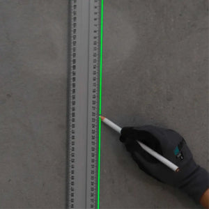 Bihui self-leveling laser level BHLLG05 projecting bright green laser line onto concrete floor next to measuring tape, held by gloved hand wearing black work glove