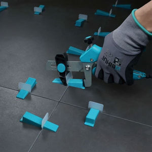 Hand holding blue and grey Bihui wedge levelling plier tool with turquoise plastic spacers and clips arranged on dark tile floor demonstrating tile levelling system