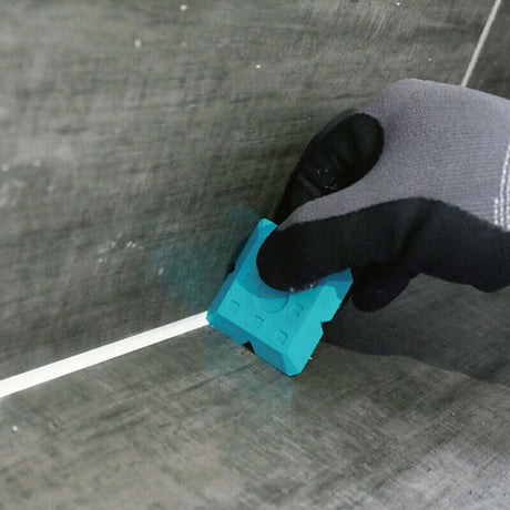 Person wearing black socks and gray pants holding a turquoise silicone caulking tool applicator against a concrete surface with white grout line