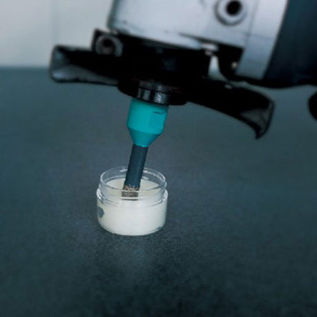 Diamond brazed tile drill bit 12mm M14 mounted on drilling machine with turquoise cooling liquid dispensing into white ceramic test sample