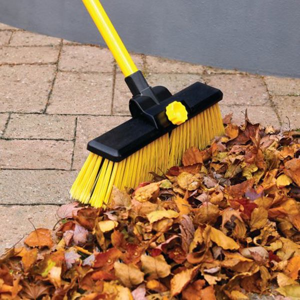 Yellow and black heavy duty broom with 14 inch brush head sweeping autumn leaves on brick paved surface
