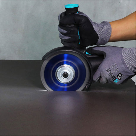 Worker wearing gray and black gloves holding a Bihui B Speedy 115mm angle grinder with spinning blue diamond cutting blade against dark surface with concrete background