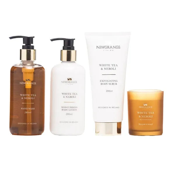 Newgrange Living White Tea and Neroli body care set containing four products including amber glass hand wash bottle, white moisturising body lotion bottle, exfoliating body scrub tube, and amber glass scented candle arranged in a row