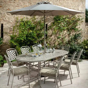 Hartman Berkeley 8 seater cast aluminium oval garden furniture set in taupe with grey cushions, featuring 6 patterned chairs and 2 armchairs around an oval table with integrated umbrella hole, complete with grey parasol, set on a stone patio against a brick wall with climbing ivy