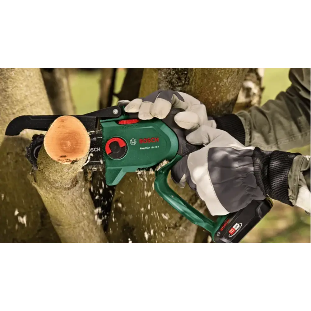 Bosch EasyChain 18V cordless chainsaw in green and black being held by gloved hands cutting through a wooden log, showing the chainsaw bar and chain in action with wood shavings flying