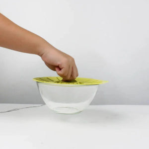 Child's hand placing a lime green silicone suction lid on a clear glass bowl demonstrating the Fresh Seal Suction Lid product functionality