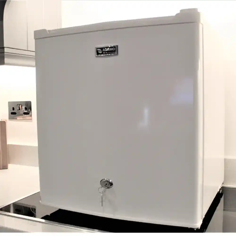 White compact tabletop refrigerator with lock feature, 46 litre capacity, Adamo brand model BC-51C, featuring stainless steel handle and security lock mechanism on front door, positioned on black base with electrical outlet visible on wall behind