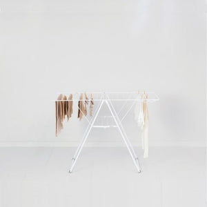 White metal winged clothes airer with beige and cream colored garments hanging on multiple bars, displayed against a white background