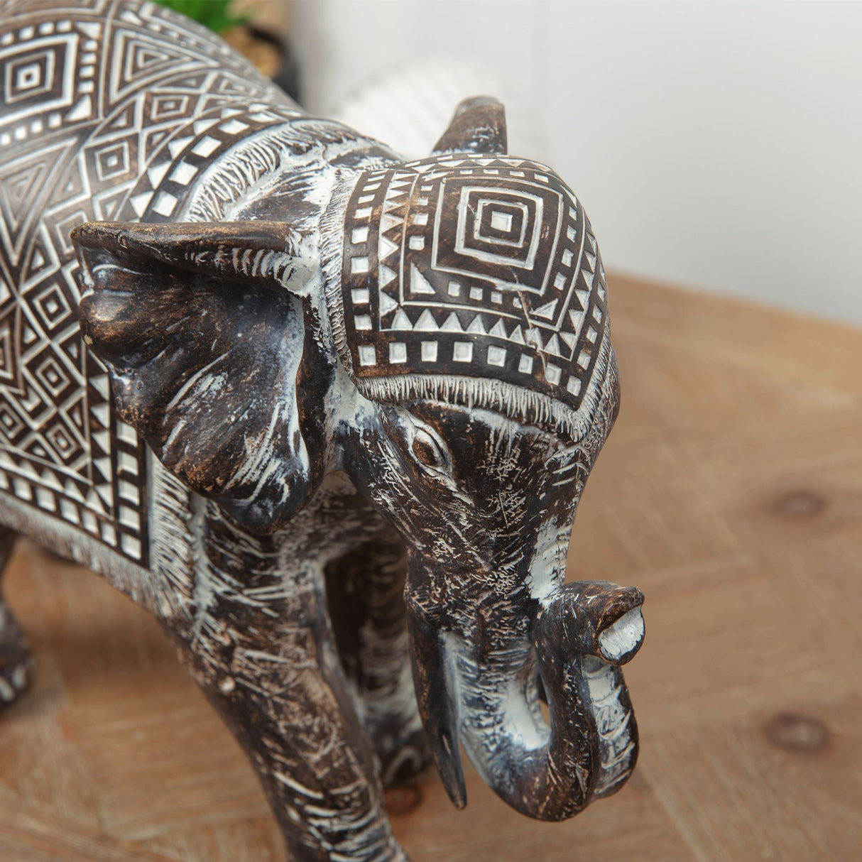 Aztec patterned elephant figurine carved from dark wood with white geometric tribal designs, featuring detailed tusks and textured body, displayed on wooden surface