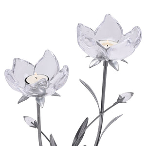 Two clear glass lotus flower candle holders with silver-toned stems and leaf details, each holding a cream-colored tea light candle, displayed against a white background