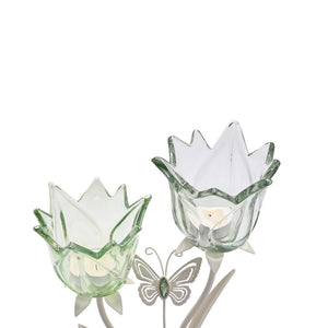 Two green glass tulip-shaped candle holders with white inner petals on a matte off-white base, accompanied by a decorative butterfly garden stake featuring green and white enamel detailing