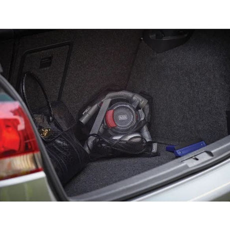 Black and Decker Dustbuster Flexi Car Vac 12V handheld vacuum in black with red accents stored in a vehicle trunk with dark carpet flooring