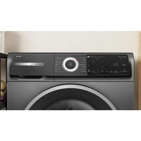 Bosch Series 6 grey front-load washing machine with 10kg capacity, 1400 spin speed, digital display panel with large central power button and control settings, model WGH254ARGB shown against white wall with wooden trim