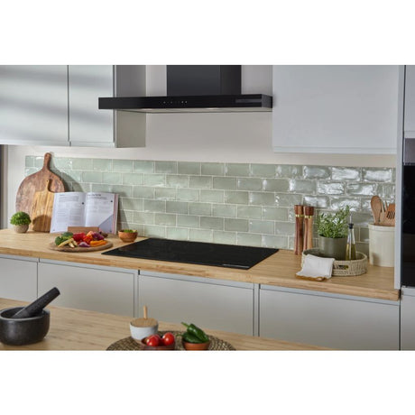 Bosch Series 6 black flex induction hob installed in modern kitchen with white cabinetry, wooden countertop, sage green subway tile backsplash, and black range hood above