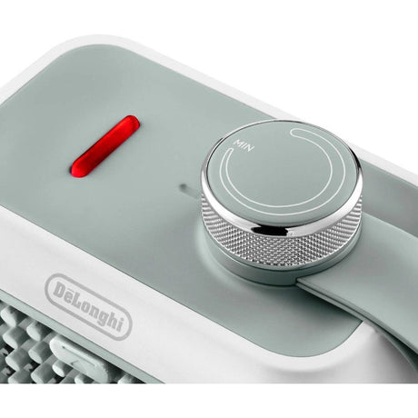DeLonghi Capsule Desk 360W Ceramic Fan Heater in sage green with chrome rotary dial control and red power indicator light, front view showing compact design with textured metal knob and white base