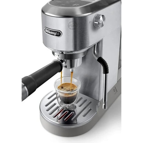 DeLonghi Dedica Duo stainless steel espresso coffee machine dispensing shot of espresso into clear glass cup on drip tray, featuring black handle and digital display