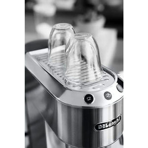 Delonghi Dedica stainless steel pump espresso machine with two clear glass cups on top and control buttons visible on the front panel in black and white product photography
