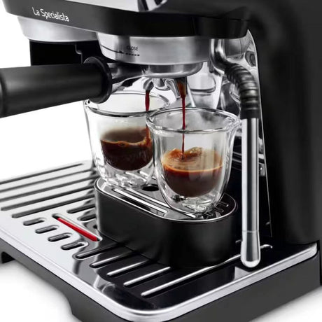 Delonghi La Specialista Arte black manual espresso machine pouring dark coffee into two glass cups on stainless steel drip tray with black handle and chrome accents