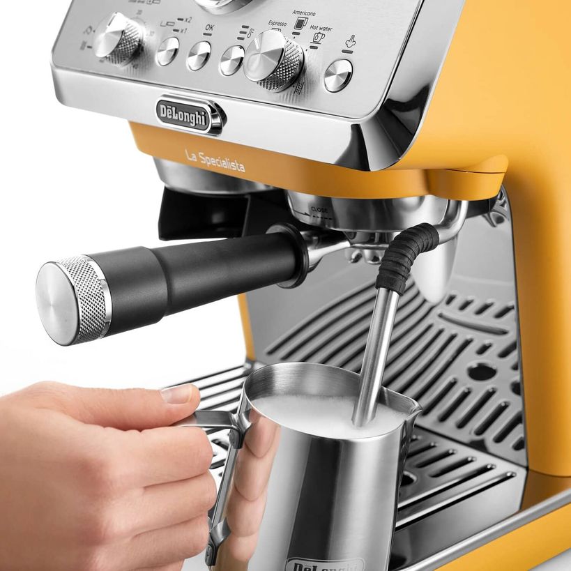 DeLonghi La Specialista Arte manual espresso machine in yellow and stainless steel with steam wand dispensing milk into metal pitcher, control panel with knobs and buttons visible