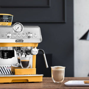 DeLonghi La Specialista Arte manual bean to cup espresso machine in yellow and stainless steel with dual espresso shots being dispensed into glass cups on wooden counter with dark background