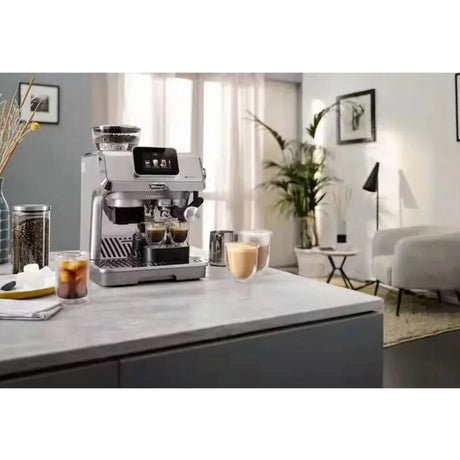 Delonghi La Specialista Touch stainless steel bean to cup coffee machine on marble kitchen counter dispensing espresso into cups, with living room and plants visible in background