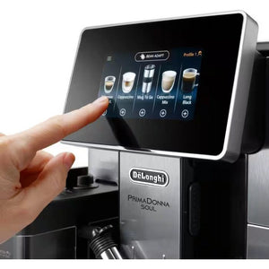 DeLonghi PrimaDonna Soul automatic coffee machine in metal black with touchscreen display showing coffee drink options including espresso, cappuccino, and long black, with a hand selecting a beverage profile