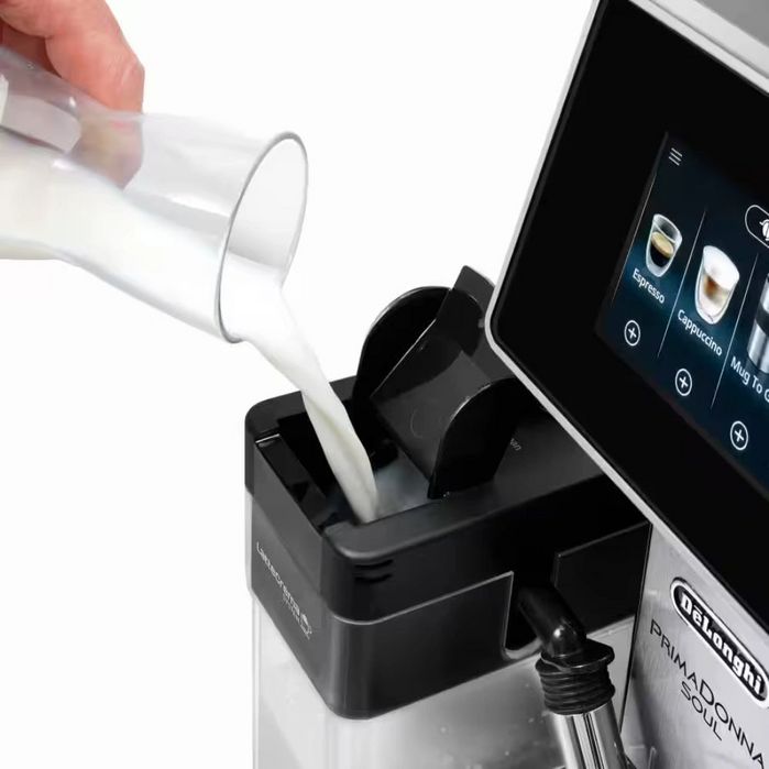 DeLonghi PrimaDonna Soul automatic espresso machine with milk frother showing milk being poured into black integrated milk system, digital touchscreen display with coffee drink selection options visible, stainless steel and black finish