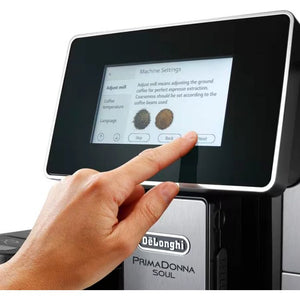 Hand touching touchscreen display of DeLonghi PrimaDonna Soul automatic coffee machine in brushed metal black finish, showing Machine Settings menu with grind adjustment options and coffee bean texture samples