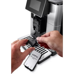Hands inserting black DeLonghi PrimaDonna Soul automatic coffee machine milk carafe into stainless steel and black machine with digital display showing product features and ease of use