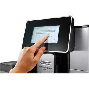 Hand touching touchscreen display of DeLonghi PrimaDonna Soul automatic coffee machine in black metal finish with stainless steel accents showing beverage selection menu