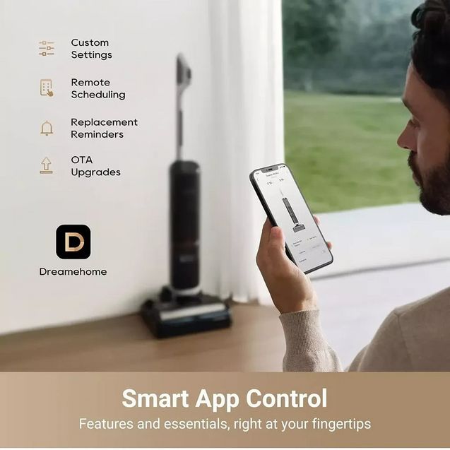 Man holding smartphone displaying Dreamehome app interface for smart vacuum control, with black Dreame H14 Pro wet and dry vacuum cleaner on wooden floor by window, showing custom settings, remote scheduling, replacement reminders and OTA upgrades features