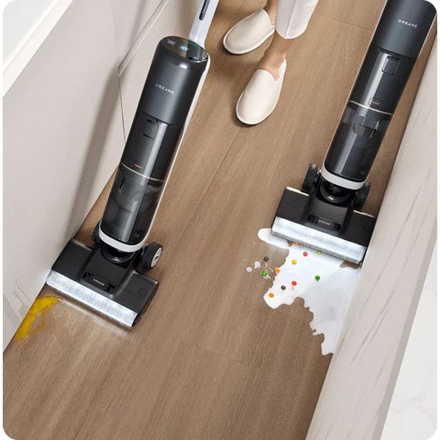Overhead view of Dreame H14 Pro wet and dry vacuum cleaner demonstrating cleaning capabilities on wooden floor with spilled colorful items and liquid, showing two black cylindrical units with white cleaning pads and a person wearing white slippers
