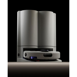 Dyson R2 Nurovi robot vacuum cleaner in silver and white with black accents, shown from front angle against black background, displaying the compact disc-shaped robotic base unit positioned in front of the tall cylindrical white docking station