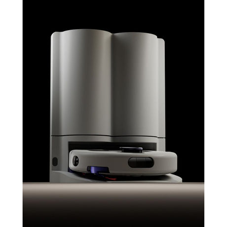 Dyson R2 Nurovi robot vacuum cleaner in silver and white with black accents, shown from front angle against black background, displaying the compact disc-shaped robotic base unit positioned in front of the tall cylindrical white docking station
