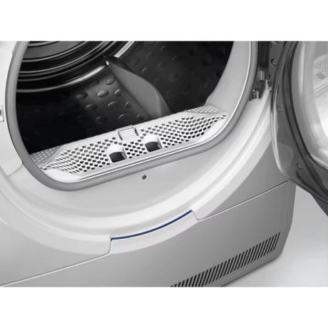 Close-up view of open white Electrolux heat pump tumble dryer showing black perforated drum interior and metal mesh lint filter tray