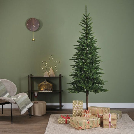 Everlands Alpbach Fir 8ft Christmas tree in sage green room setting with wrapped gifts, wooden shelving unit, wall clock and modern home decor