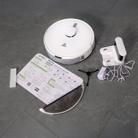 White HomeBot Spritz robot vacuum with circular disc design, shown from above on grey tiled floor alongside instruction manual, cleaning brush, mop pad attachment, and white charging dock with coiled power cable