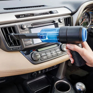 Hand holding blue and black JML Go Vac portable handheld vacuum cleaner inside car dashboard with beige interior and climate controls visible