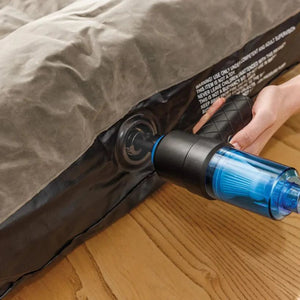 Person holding JML Go Vac portable handheld vacuum cleaner with blue water tank attachment over wooden floor next to bed with grey bedding