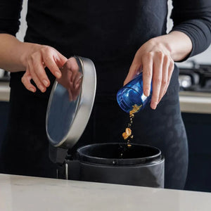 Person in black clothing pouring golden debris from a blue container into a black JML Go Vac portable handheld vacuum cleaner with white lid, demonstrating the product's dustbin emptying feature on a white surface