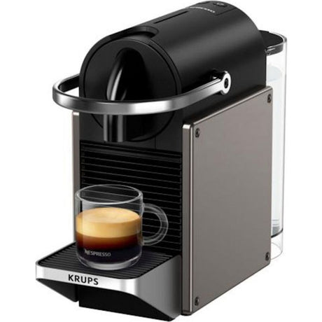 Krups Pixie Nespresso pod coffee machine in black and titanium with chrome accents, featuring a 0.7 litre water tank, compact design, and freshly brewed espresso in glass cup on drip tray