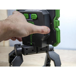 Hand holding green and black rechargeable work light with LED display and tripod stand base on wooden surface
