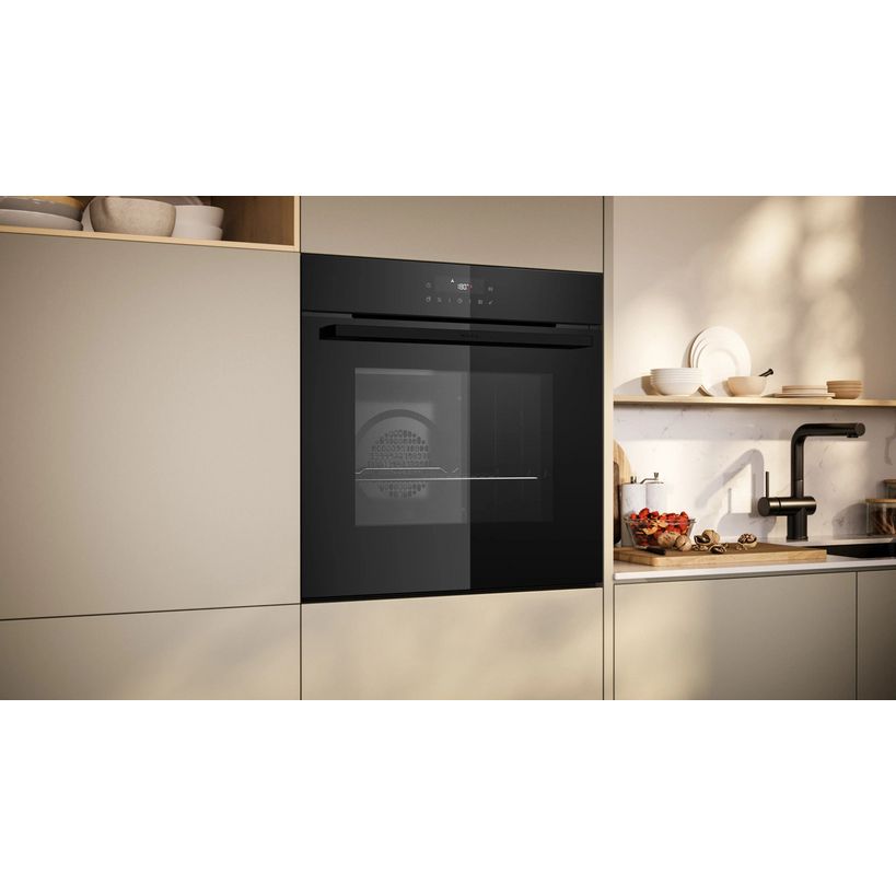 Neff N30 black pyrolytic single built-in oven integrated into beige kitchen cabinetry with open shelving displaying kitchenware and a black tap
