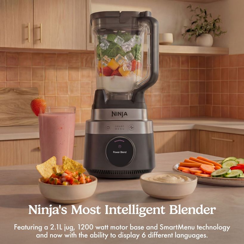 Ninja CrushBOSS intelligent blender with stainless steel and black base featuring 2.1L jug containing ice, strawberries and mint, displayed on kitchen counter surrounded by fresh ingredients including strawberry smoothie, diced vegetables and fresh produce in bowls