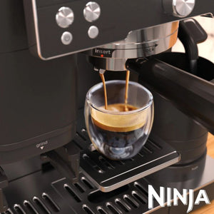 Ninja Luxe Café Premier Series black espresso machine dispensing dark coffee with crema into a double-walled glass cup, featuring stainless steel accents and control panel with settings buttons