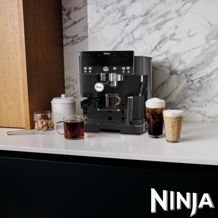Black Ninja Luxe Café Premier Series coffee machine on white marble countertop displaying multiple beverage options including espresso, cold brew, and cappuccino, with marble backsplash and wooden cabinetry