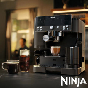 Ninja Luxe Café Premier Series black espresso machine with stainless steel accents dispensing coffee into a cup, displayed with a black mug and cold beverage glass on a dark counter in a modern kitchen setting