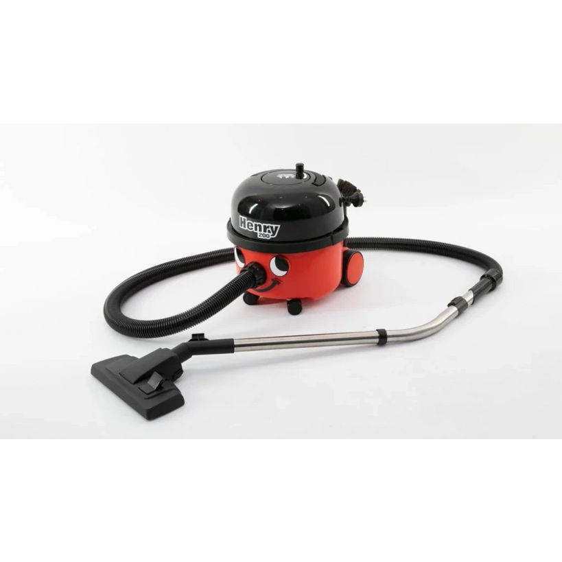 Numatic Henry compact vacuum cleaner with red and black body, featuring black dome-shaped top, flexible hose with metal wand attachment and black floor brush head on white background
